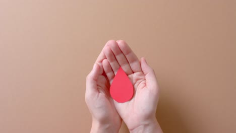 Hands-of-caucasian-woman-holding-blood-drop-on-beige-background-with-copy-space,-slow-motion