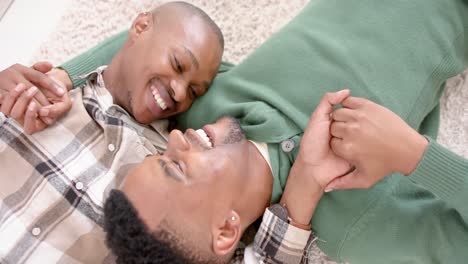 Happy-african-american-gay-male-couple-lying-on-floor,-embracing-and-smiling,-slow-motion