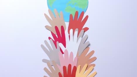 Close-up-of-hands-together-with-globe-made-of-colourful-paper-on-white-background-with-copy-space