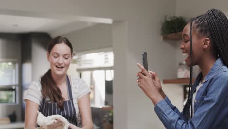 Happy-diverse-teenage-female-friends-making-dough-and-using-smartphone-in-slow-motion