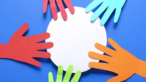 Close-up-of-hands-touching-circle-made-of-colourful-paper-on-blue-background-with-copy-space