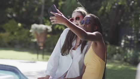 Fröhliche,-Vielfältige-Teenager-Freundinnen-Mit-Sonnenbrille,-Die-In-Zeitlupe-Ein-Selfie-Im-Garten-Am-Pool-Machen