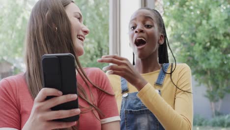 Shocked-diverse-teenage-female-friends-lying-on-couch-and-using-smartphones-in-slow-motion