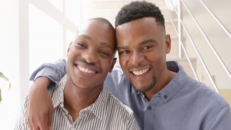 Portrait-of-happy-african-american-gay-male-couple-sitting-on-stairs-and-embracing,-slow-motion