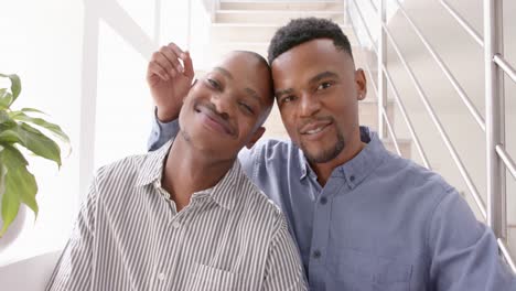 Portrait-of-happy-african-american-gay-male-couple-sitting-on-stairs-and-embracing,-slow-motion