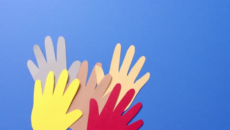 Close-up-of-hands-together-made-of-colourful-paper-on-blue-background-with-copy-space