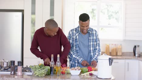Happy-african-american-gay-male-couple-preparing-dinner,-chopping-vegetables-in-kitchen,-slow-motion