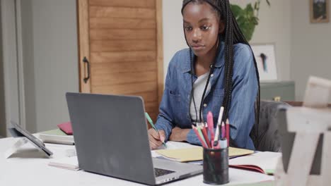 Fokussiertes-Afroamerikanisches-Teenager-Mädchen,-Das-Zu-Hause-Mit-Einem-Laptop-Am-Esstisch-Lernt