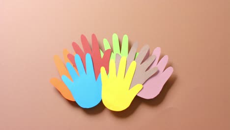 Close-up-of-hands-together-made-of-colourful-paper-on-brown-background-with-copy-space