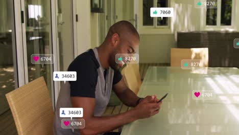 Animation-of-social-media-icons-floating-against-african-american-man-using-smartphone-at-home