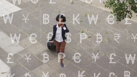 Animation-of-currency-symbols-over-african-american-businesswoman-talking-on-smartphone-on-street