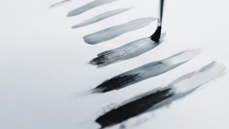 Close-up-of-brush-painting-stripes-with-black-paint-on-white-background,-slow-motion