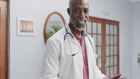 Portrait-of-african-american-male-doctor-wearing-lab-coat-and-stethoscope,-using-tablet,-slow-motion