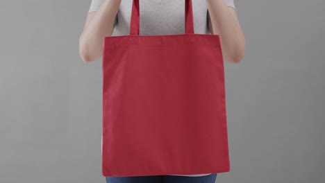 Kaukasische-Frau-Trägt-Weißes-T-Shirt-Mit-Roter-Tasche-Auf-Grauem-Hintergrund,-Kopierraum,-Zeitlupe