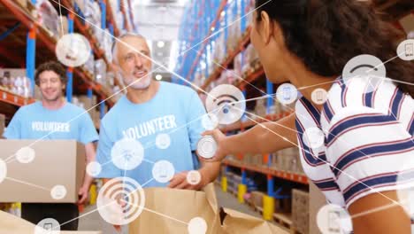 Animation-of-network-of-digital-icons-over-biracial-woman-donating-groceries-to-male-volunteer