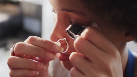 Biracial-female-worker-inspecting-ring-with-magnifying-glass-in-workshop-in-slow-motion