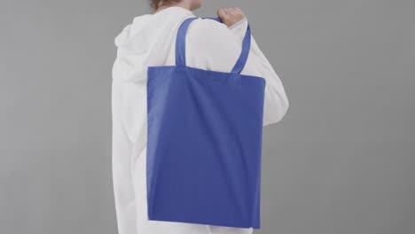Caucasian-woman-wearing-white-hoodie-holding-blue-bag-on-grey-background,-copy-space,-slow-motion