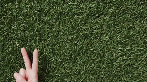 Close-up-of-hand-of-caucasian-woman-showing-peace-sign-with-copy-space-on-grass-background