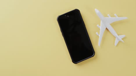 Close-up-of-white-plane-model,-smartphone-and-copy-space-on-yellow-background