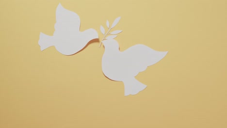 Close-up-of-white-doves-with-leaf-and-copy-space-on-yellow-background