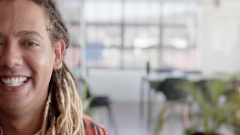 Portrait-of-happy-biracial-casual-businessman-with-dreadlocks-in-office-with-copy-space,-slow-motion