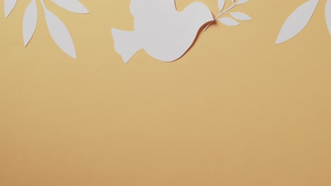 Close-up-of-white-dove-with-leaves-and-copy-space-on-yellow-background