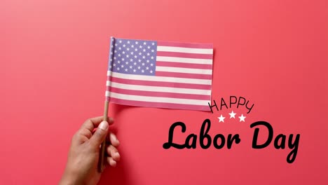 Animation-Des-Textes-„Happy-Labor-Day“-Und-Der-Hand,-Die-Die-Flagge-Der-USA-Auf-Rotem-Hintergrund-Hält