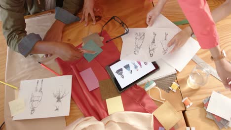 Diverse-designers-working-at-table-with-tablet-and-fashion-drawings-in-fashion-studio,-slow-motion