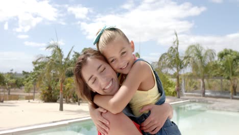 Portrait-of-happy-caucasian-mother-carrying-daughter-at-swimming-pool-at-beach-house