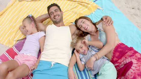 Portrait-of-happy-caucasian-family-lying-on-towels-at-beach