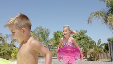 Happy-caucasian-siblings-running-with-inflatables-at-beach-house