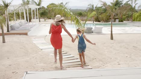 Caucasian-mother-with-daughter-running-and-holding-hands-at-beach-house