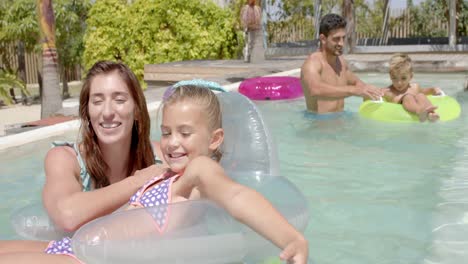 Portrait-of-happy-caucasian-family-playing-with-inflatables-in-swimming-pool