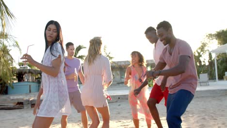 Happy-diverse-group-of-friends-dancing-holding-cocktails-at-beach