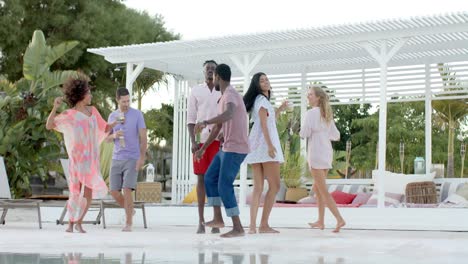 Happy-diverse-group-of-friends-dancing-holding-cocktails-by-swimming-pool