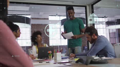 Animation-of-digital-icons-against-african-american-man-talking-to-diverse-colleagues-at-office