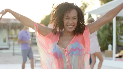 Portrait-of-happy-biracial-woman-dancing-with-friends-at-beach