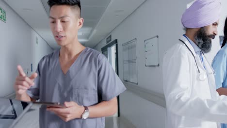 Diverse-doctors-and-nurses-using-tablets-and-walking-through-corridor-at-hospital,-in-slow-motion