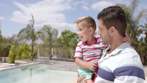 Happy-caucasian-father-carrying-son-at-swimming-pool-at-beach-house