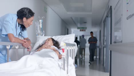 Diverse-female-doctor-and-child-patient-talking-in-corridor-at-hospital,-in-slow-motion