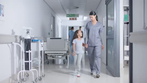 Diverse-female-nurse-and-child-patient-walking-through-corridor-at-hospital,-in-slow-motion