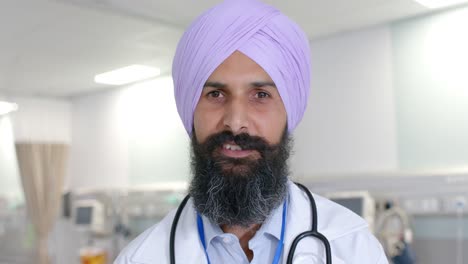 Portrait-of-happy-biracial-sikh-male-doctor-in-turban-looking-at-camera-at-hospital,-in-slow-motion