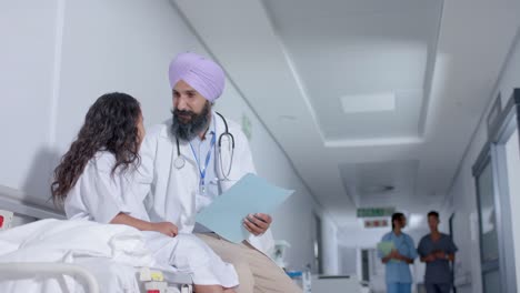 Diverse-sikh-male-doctor-in-turban-and-child-patient-talking-in-corridor-at-hospital,-in-slow-motion