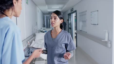 Diverse-doctor-and-nurse-using-tablets-and-talking-in-corridor-at-hospital,-in-slow-motion