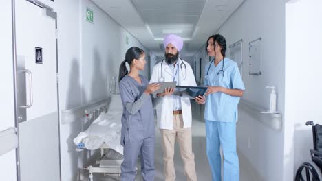 Diverse-doctors-and-nurse-using-tablet-and-walking-through-corridor-at-hospital,-in-slow-motion