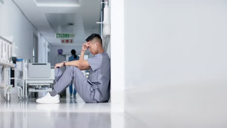 Stressed-asian-male-surgeon-sitting-and-leaning-on-wall-in-hospital-in-slow-motion