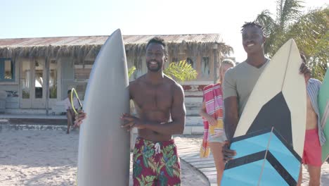 Happy-diverse-friends-with-surfboards-talking-over-beach-house