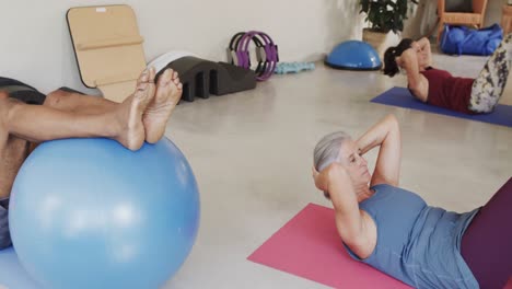 Diverse-seniors-using-exercise-balls-in-pilates-class-with-female-coach,-unaltered,-in-slow-motion