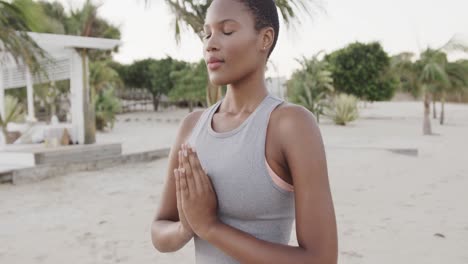 Relaxed-biracial-woman-practicing-yoga,-meditating-on-beach,-slow-motion
