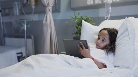 Happy-biracial-sick-girl-patient-using-tablet-in-hospital-bed-in-slow-motion